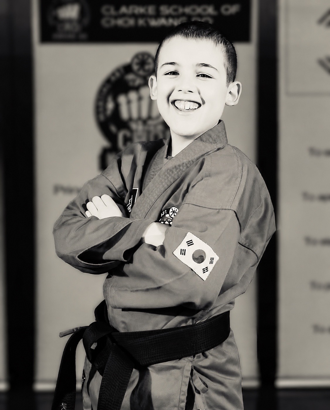 A smiling young student in a Choi Kwang Do uniform with a black belt, arms folded
